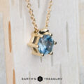 The BYO "Zephyr" necklace in 14K yellow gold, featuring a 0.66-carat hexagon Montana sapphire pendant, is displayed on a light wooden background. The Earth's Treasury logo is shown at the bottom.