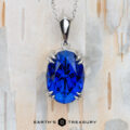 The "Aria" pendant in platinum with an 8.05-carat Royal Blue Tanzanite is shown on a light wood background, with the text "EARTH'S TREASURY" displayed below.