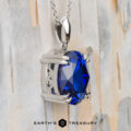 The "Aria" pendant in platinum with an 8.05-carat Royal Blue Tanzanite is shown on a light wood background, with the text "EARTH'S TREASURY" displayed below.