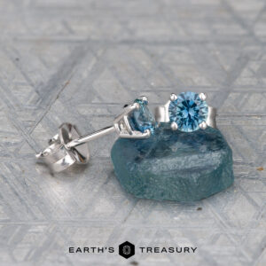 The EA-MS-402 4.0mm silver stud earrings feature round blue gemstones, shown on a rough blue stone with a patterned gray background.