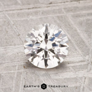 A 1.37-carat heated Ceylon sapphire with a round brilliant cut is displayed on a textured gray surface, featuring the Earth's Treasury logo at the bottom.