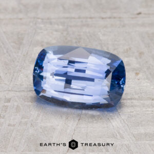 A 2.02-carat Ceylon sapphire in a rectangular cushion cut is shown on a textured gray surface with "EARTH'S TREASURY" displayed beneath.