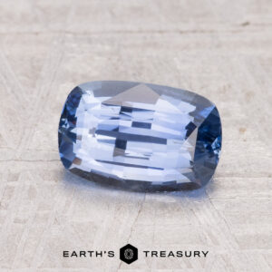 A 2.02-carat Ceylon sapphire in a rectangular cushion cut is shown on a textured gray surface with "EARTH'S TREASURY" displayed beneath.