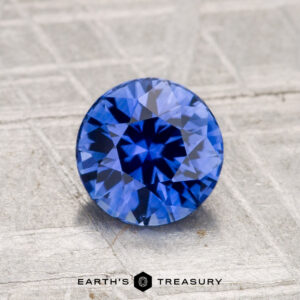 A 1.40-carat heated Ceylon sapphire is displayed on a textured, light gray surface with "Earth's Treasury" branding below.