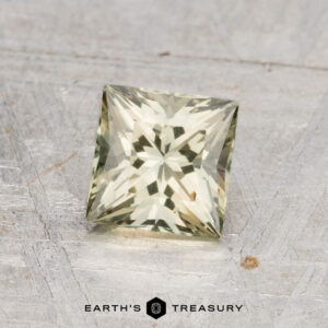 A square-cut, pale yellow 1.14-carat heated Australian sapphire with faceted surfaces is displayed on a textured metallic background, with the "Earth's Treasury" logo at the bottom.