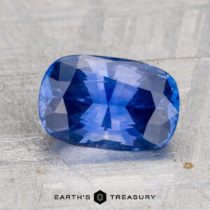 A 2.92-carat Ceylon sapphire, faceted and rectangular, is displayed on a light textured surface with "EARTH'S TREASURY" and a hexagon logo visible at the bottom.