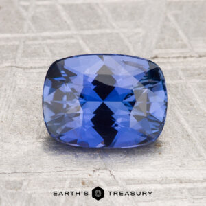 A 2.08-carat Ceylon sapphire with a cushion cut sits on a textured surface, with the "Earth’s Treasury" logo displayed at the bottom.