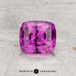 A 1.54-carat heated Ceylon sapphire in cushion cut, showcased on a light textured surface with "EARTH'S TREASURY" at the bottom.