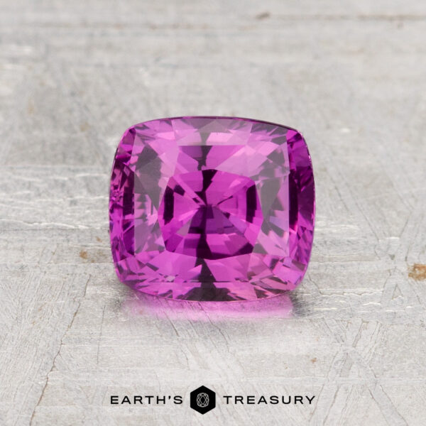 1.54-Carat Ceylon Sapphire (Heated) A 1.54-carat heated Ceylon sapphire in cushion cut, showcased on a light textured surface with "EARTH'S TREASURY" at the bottom.