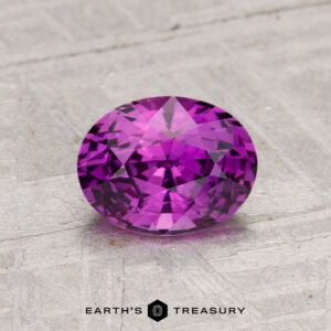 A 1.37-Carat Ceylon Sapphire (Heated), round and faceted, is shown on a textured light gray surface with "EARTH'S TREASURY" beneath it.