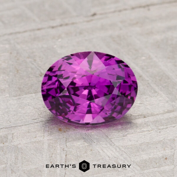 1.37-Carat Ceylon Sapphire (Heated) A 1.37-Carat Ceylon Sapphire (Heated), round and faceted, is shown on a textured light gray surface with "EARTH'S TREASURY" beneath it.