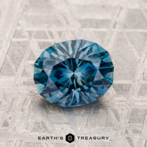 A 1.55-carat Montana sapphire rests on a textured surface with the text "Earth's Treasury" below it.