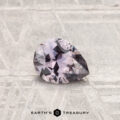 A 0.68-carat Montana sapphire, pear-shaped and faceted with a light purple hue, rests on a textured metallic surface. "EARTH'S TREASURY" appears at the bottom.