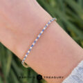 A close-up of a wrist wearing product _DSC1650-1200-BW, a delicate tennis bracelet with alternating blue and white stones; Earth's Treasury logo at the bottom.