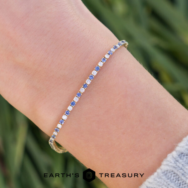 The "Analise" Bracelet On Hand A close-up of a wrist wearing product _DSC1650-1200-BW, a delicate tennis bracelet with alternating blue and white stones; Earth's Treasury logo at the bottom.