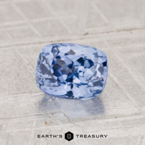 A 1.50-carat faceted Ceylon Sapphire rests on a textured surface, with the "EARTH'S TREASURY" logo displayed at the bottom of the image.