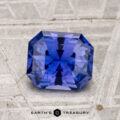 A 1.63-carat Ceylon sapphire with an emerald cut is displayed on a textured gray surface, with "Earth's Treasury" shown below.