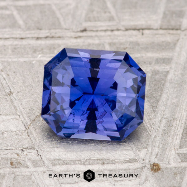 1.63-Carat Ceylon Sapphire A 1.63-carat Ceylon sapphire with an emerald cut is displayed on a textured gray surface, with "Earth's Treasury" shown below.