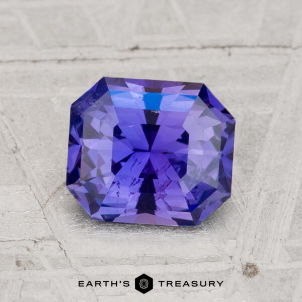 1.63-Carat Ceylon Sapphire A faceted, rectangular 1.63-Carat Ceylon Sapphire in violet-blue is shown on a light textured surface with "EARTH'S TREASURY" beneath.