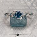 The "Aralia" ring in platinum featuring a 1.03-carat Montana sapphire and leaf motifs is displayed on a rough blue stone, with the Earth's Treasury logo at the bottom.