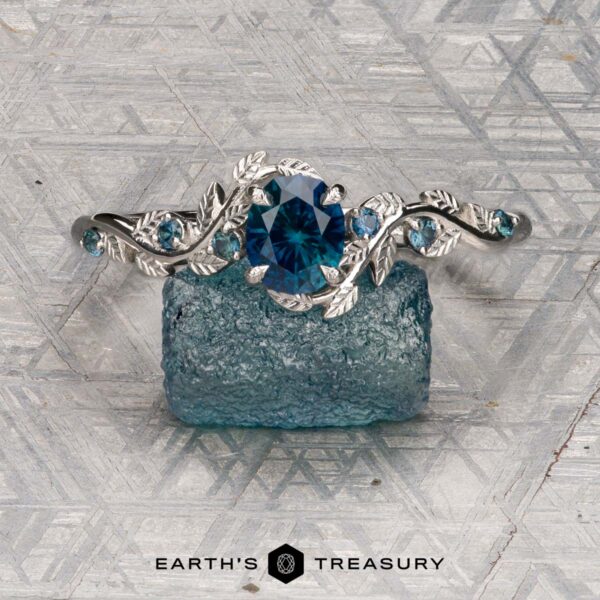 The "Aralia" ring in platinum with 1.03-carat Montana sapphire The "Aralia" ring in platinum featuring a 1.03-carat Montana sapphire and leaf motifs is displayed on a rough blue stone, with the Earth's Treasury logo at the bottom.
