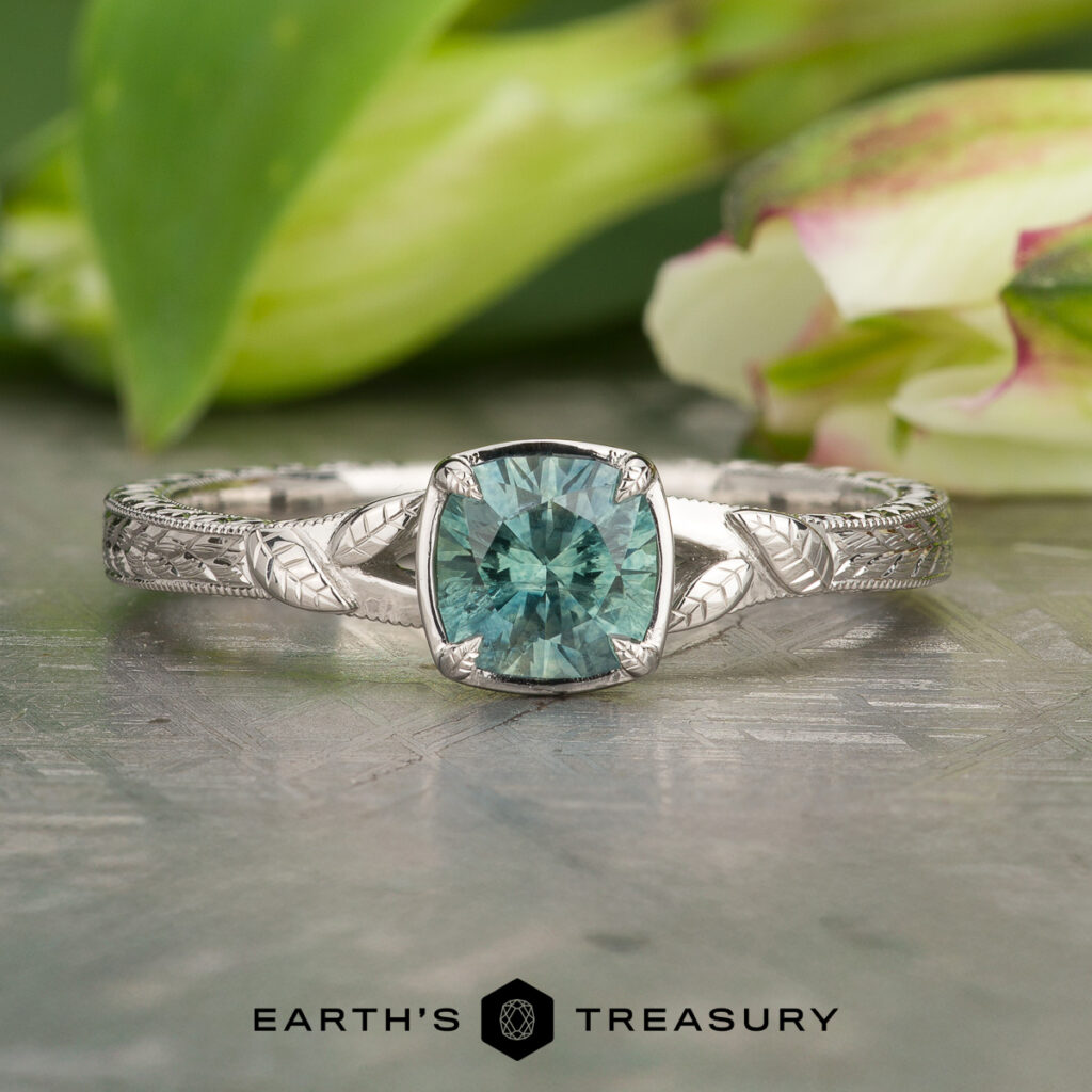 The ring "Stacked from 15 images. Method=B (R=14,S=2)" features an intricate silver band and a square-cut teal gemstone, shown on a reflective surface with green leaves and a white flower in the background.