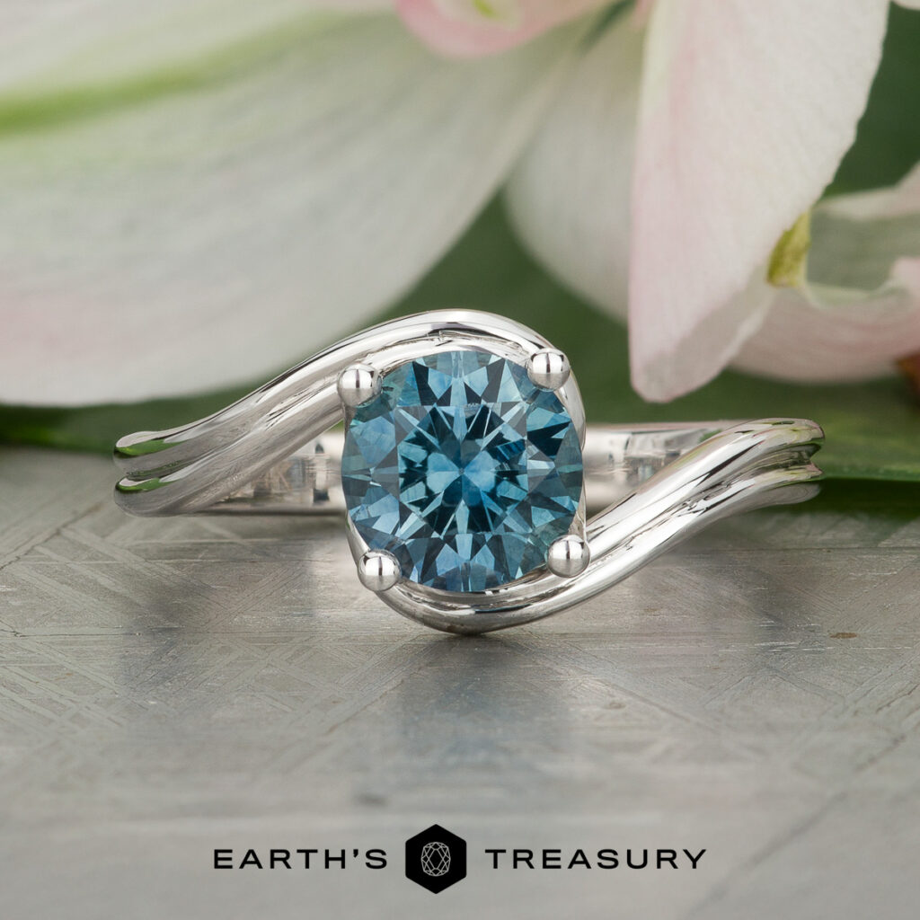 A silver ring with a round blue gemstone, "Stacked from 14 images. Method=B (R=14,S=2)", is displayed on a textured surface with pink and white flower petals in the background and "EARTH'S TREASURY" at the bottom.