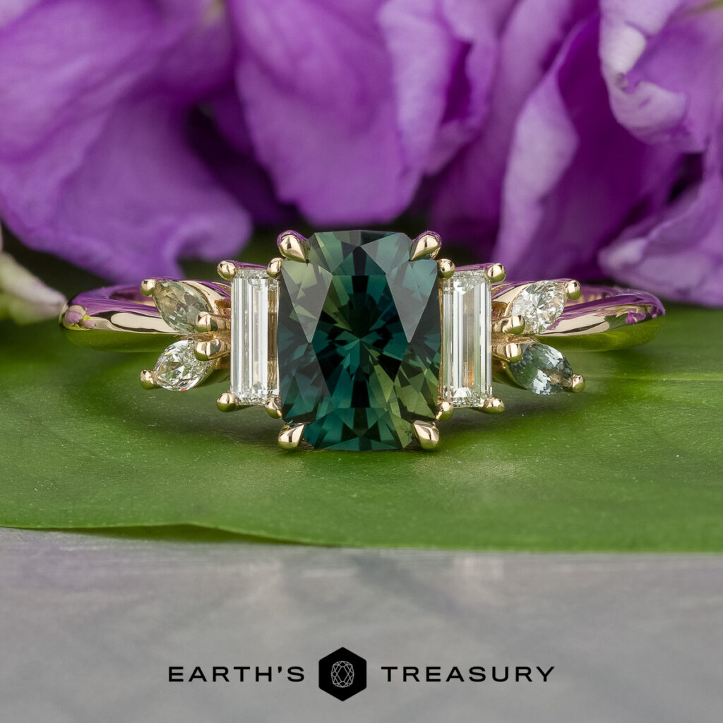 The "Stacked from 14 images. Method=B (R=14,S=1)" gold ring features a rectangular green gemstone at the center, accented by baguette and marquise-cut diamonds, shown on a green surface with purple flowers in the background.