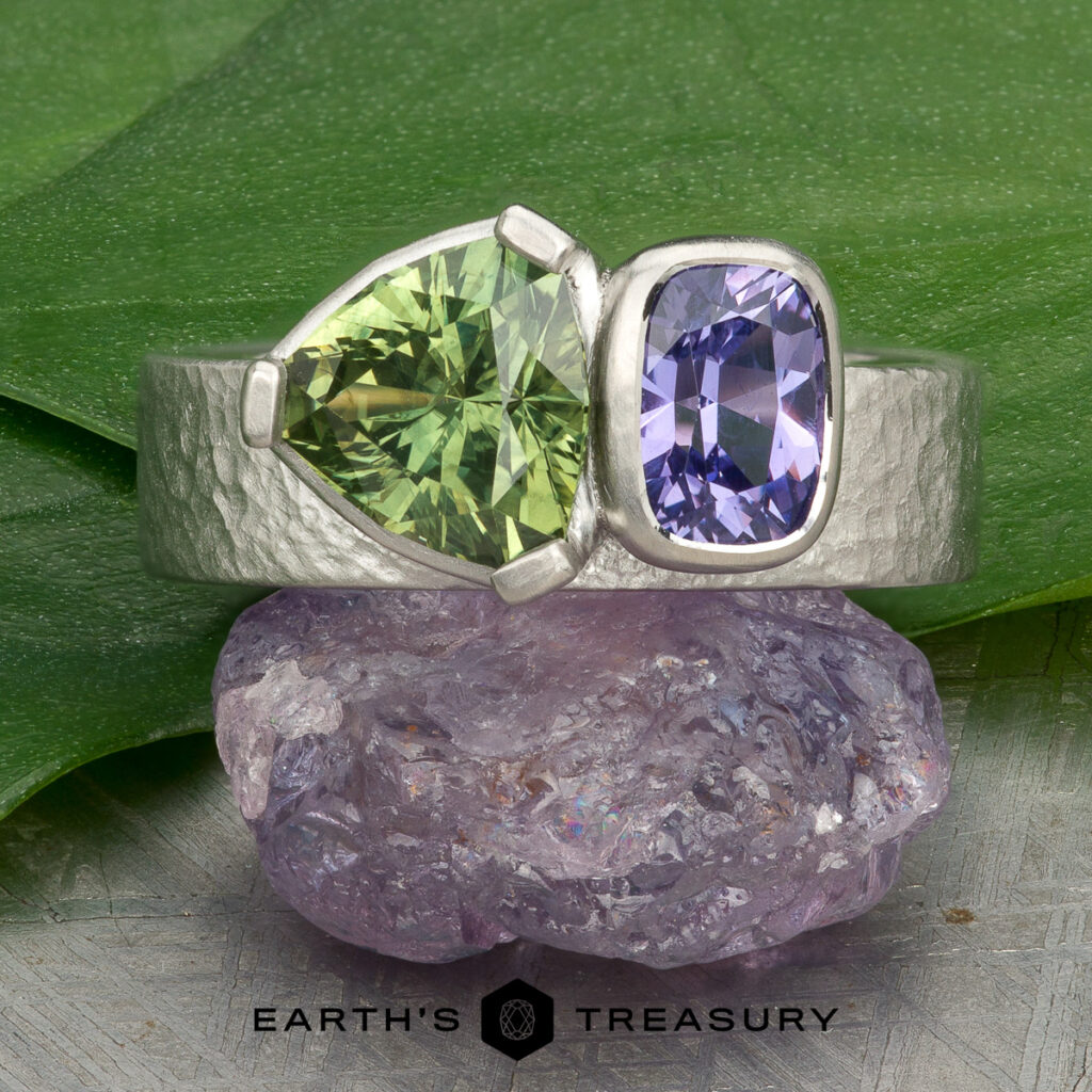 Stacked from 38 images. Method=B (R=14,S=2): A silver ring with green and purple gemstones displayed on raw purple crystal, set against a green leaf background.