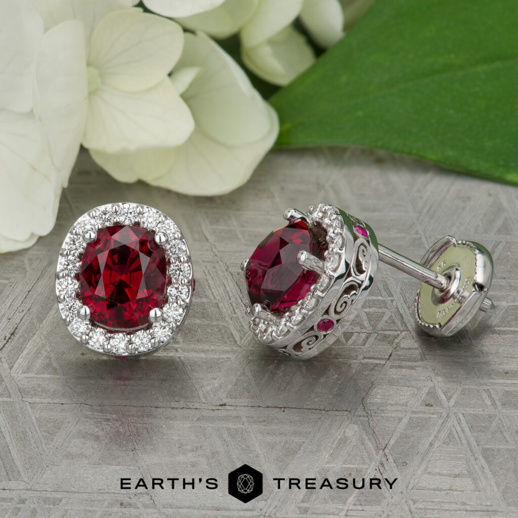 A pair of round red gemstone stud earrings with diamond halos set in silver, displayed on a patterned surface near white flowers. "Earth's Treasury" logo and the product "Stacked from 15 images. Method=B (R=14,S=2)" are at the bottom.
