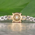 Close-up of The "Araceli" Bracelet in 14K white and yellow gold, featuring a 2.96-carat spinel and a central ornate round design, displayed on a reflective surface with a green leaf background—ideal for bracelet stacking.