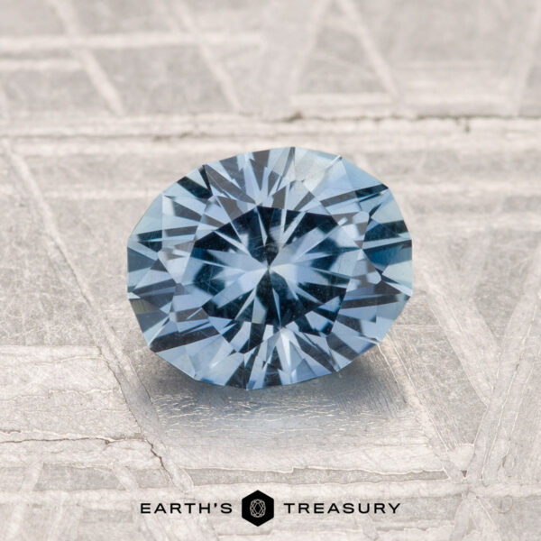 1.38-Carat Montana Sapphire A 1.38-carat Montana sapphire with faceted blue hues is displayed on a textured gray surface, with the Earth's Treasury logo beneath it.