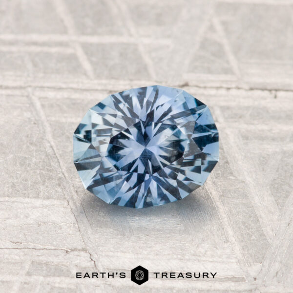 1.13-Carat Montana Sapphire A 1.13-carat Montana sapphire with an oval facet rests on a textured metallic surface, with "Earth's Treasury" inscribed below.