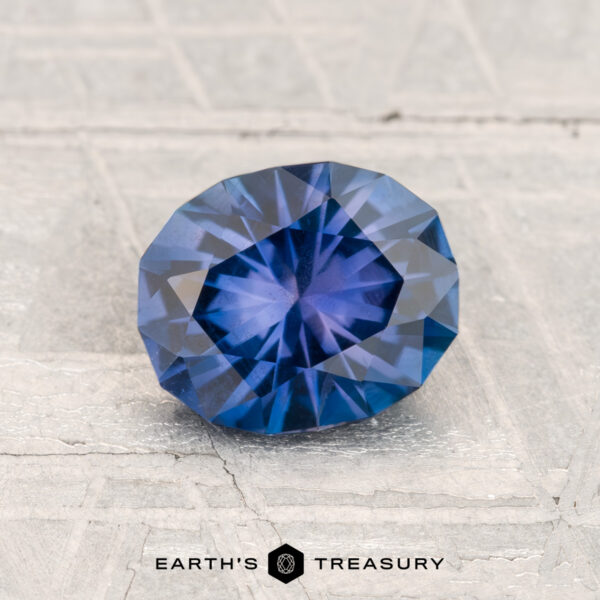 1.27-Carat Montana Sapphire A 1.27-carat Montana Sapphire, oval and blue, rests on a textured light surface with the "Earth's Treasury" text and logo displayed below.