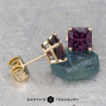A pair of 6.2mm Deep Purple Spinel earrings in gold settings, one displayed upright on a rough stone, with the Earth's Treasury logo at the bottom.