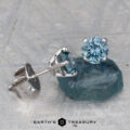 A pair of 5.25mm light aqua Montana sapphire stud earrings (heated) set in silver, displayed on a rough blue-green stone with the "Earth's Treasury" logo at the bottom.