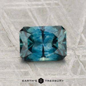 1.67-carat step-cut blue-green Montana sapphire (heated) displayed on textured gray surface; "Earth's Treasury" logo at the bottom.
