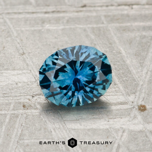 1.02-Carat Montana Sapphire (Heated) A 1.02-carat heated Montana sapphire with a blue hue is displayed on a textured, light-colored surface above the "Earth's Treasury" logo.