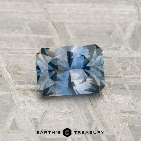 0.90-Carat Montana Sapphire (Heated) A 0.90-carat rectangular, faceted Montana sapphire (heated) is displayed on a textured gray surface with "Earth's Treasury" at the bottom.