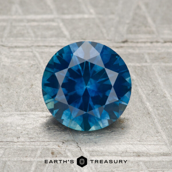 1.49-Carat Montana Sapphire (Heated) A 1.49-carat faceted Montana sapphire (heated) is displayed on a textured gray surface with "Earth's Treasury" at the bottom.
