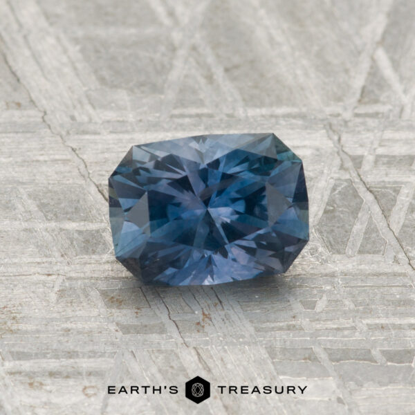 1.04-Carat Montana Sapphire (Heated) A 1.04-carat heated Montana sapphire with a cushion cut rests on a textured gray metallic surface, featuring the text "Earth's Treasury" below.