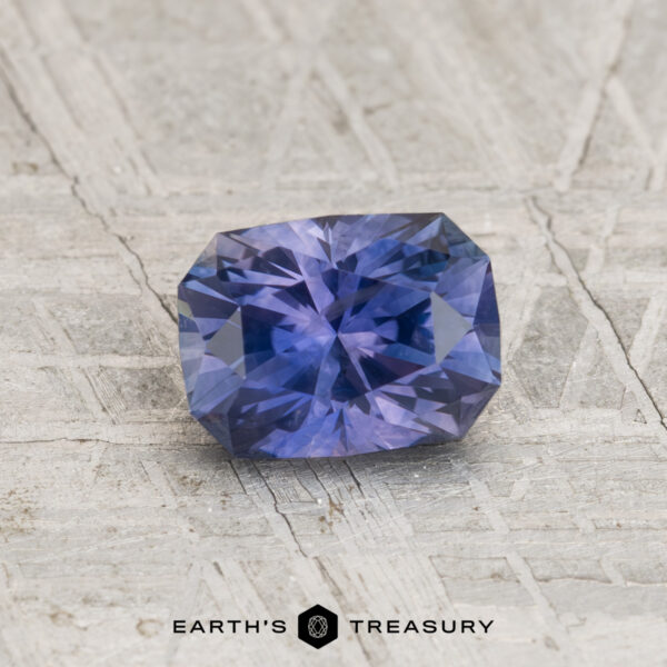 1.04-Carat Montana Sapphire (Heated) A 1.04-carat heated Montana sapphire in a rectangular cushion cut rests on a textured, light-colored surface with the Earth's Treasury logo at the bottom of the image.