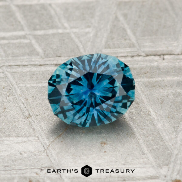 0.97-Carat Montana Sapphire (Heated) A 0.97-carat heated Montana Sapphire, brilliant-cut in teal, displayed on a metallic textured surface with "Earth's Treasury" beneath.