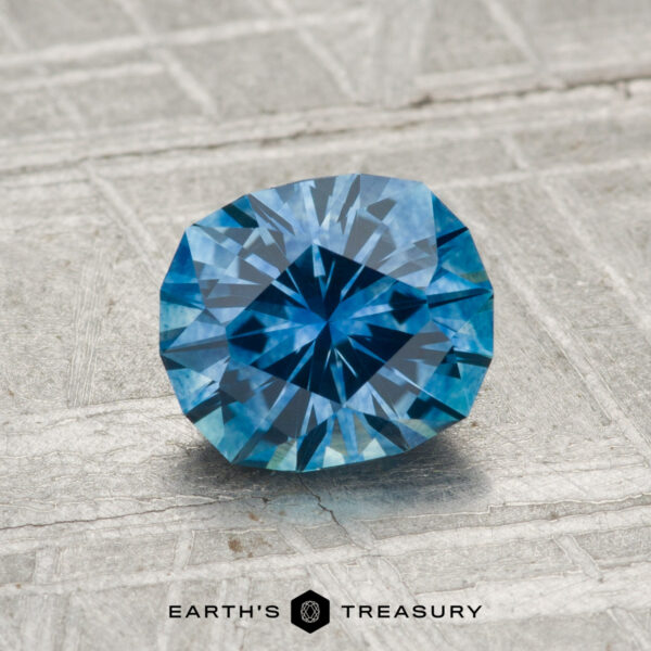 1.37-Carat Montana Sapphire (Heated) A 1.37-carat heated Montana sapphire with an oval cut rests on a textured gray surface; the "Earth's Treasury" logo appears at the bottom.