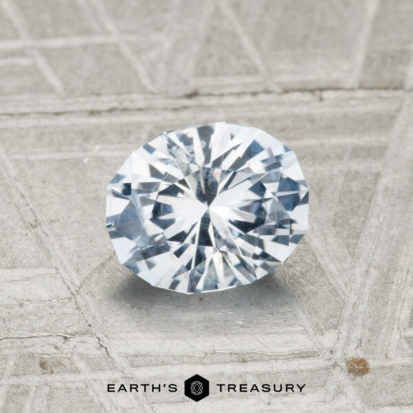 1.11-Carat Montana Sapphire A 1.11-Carat Montana Sapphire gemstone glimmers on a textured gray surface, with “EARTH’S TREASURY” and a hexagonal logo beneath.