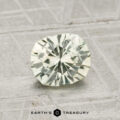 A 1.25-Carat Montana Sapphire, light green and faceted, rests on a textured gray surface with "EARTH'S TREASURY" displayed at the bottom.