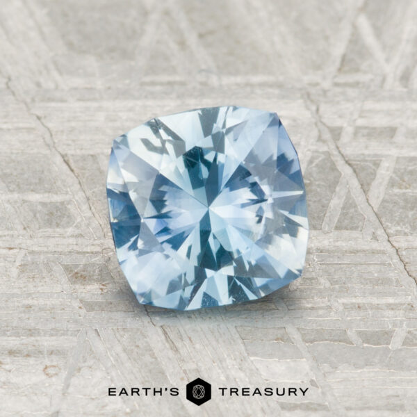 1.23-Carat Montana Sapphire (Heated) A 1.23-carat cushion-cut Montana sapphire (heated) displayed on a textured gray surface, with the text "EARTH'S TREASURY" below.