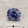A 1.18-carat heated Montana sapphire rests on a textured gray surface with the text “EARTH'S TREASURY” displayed below.