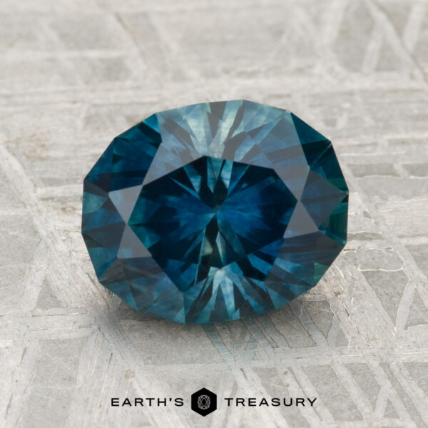 2.71-Carat Montana Sapphire (Heated) A round, faceted 2.71-carat heated Montana sapphire is displayed on a textured gray surface with "EARTH'S TREASURY" at the bottom.
