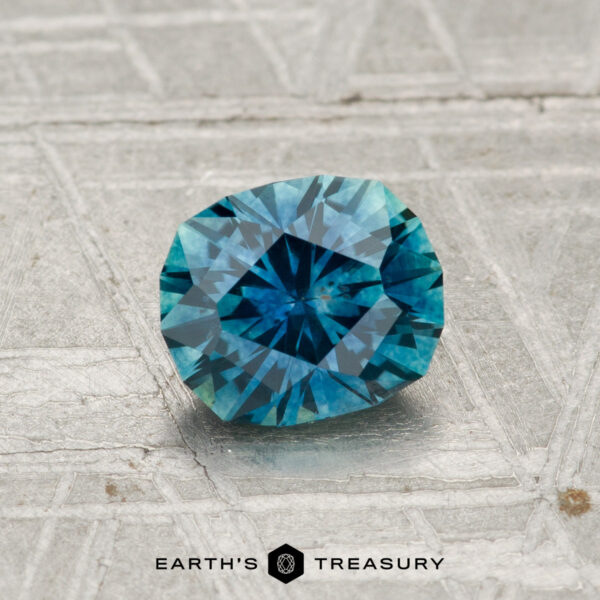 1.08-Carat Montana Sapphire (Heated) A 1.08-carat heated Montana sapphire with teal-blue highlights rests on a patterned metallic surface, with the text "Earth's Treasury" at the bottom.